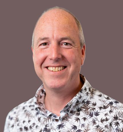 Lachende man in een overhemd met patroon tegen een effen grijze achtergrond.