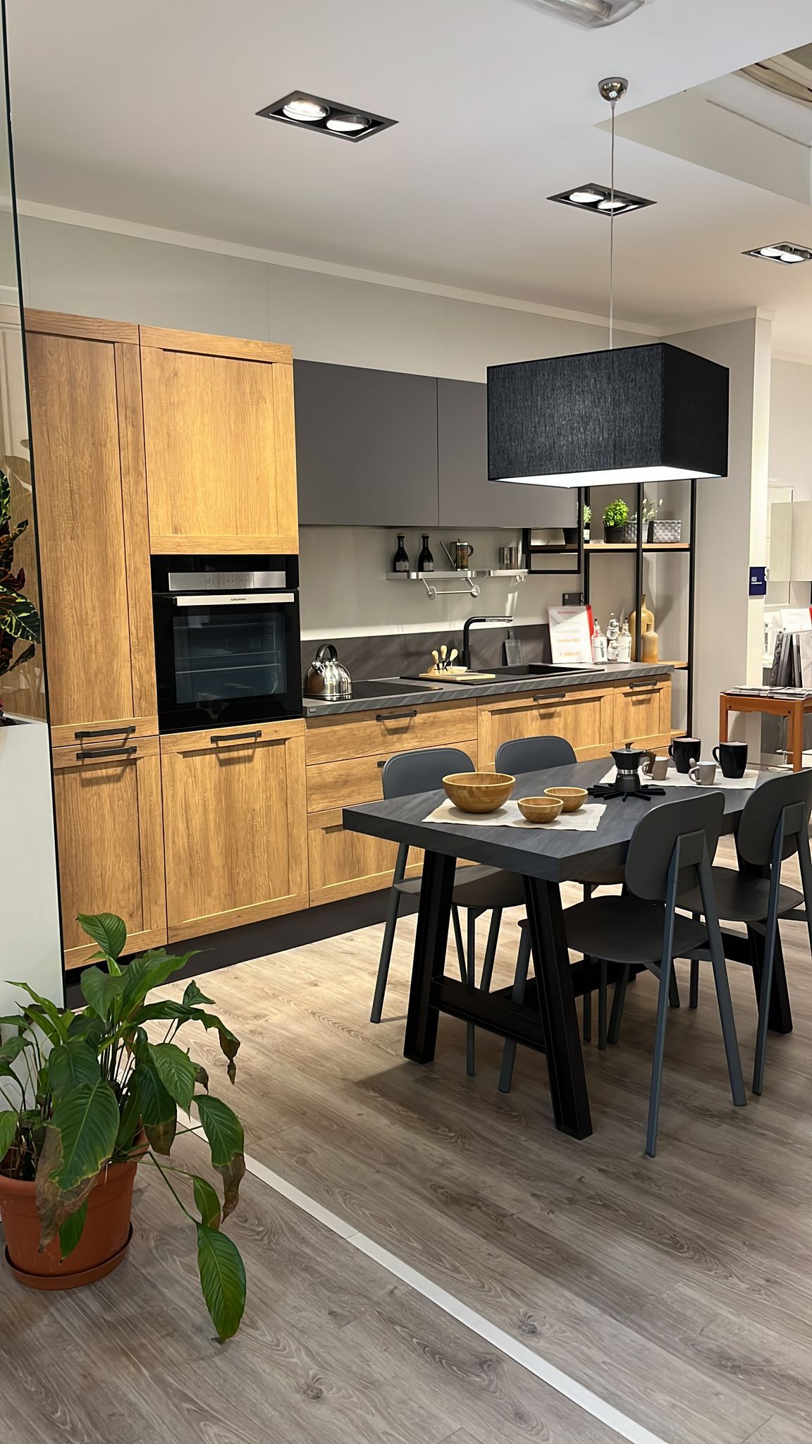 Una cucina e zona pranzo moderna con mobili in legno chiaro, ripiani grigi, tavolo da pranzo coordinato e posti a sedere.