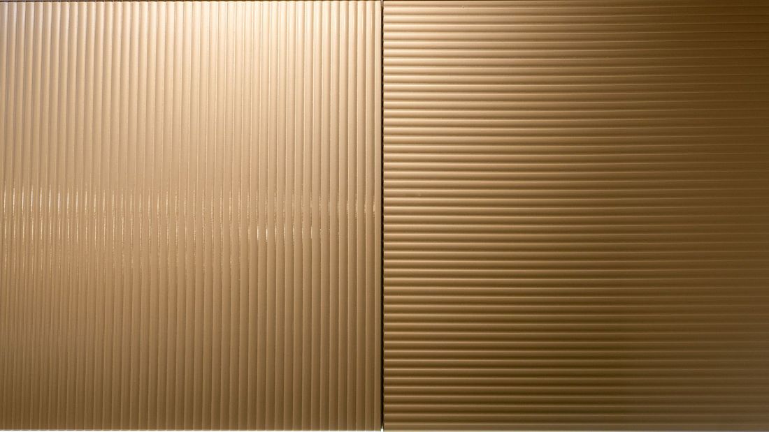 Due pannelli verticali affiancati con superfici identiche in bronzo metallico: uno caratterizzato da nervature verticali, l'altro orizzontali.