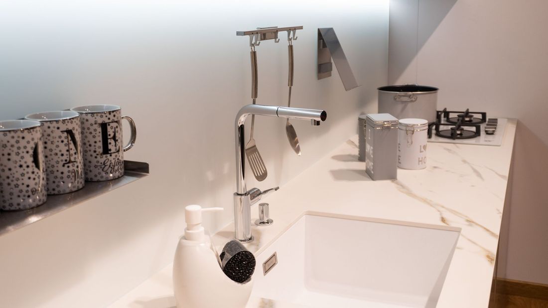 Una moderna zona lavello da cucina con rubinetto cromato, piano di lavoro bianco, contenitori decorati e utensili da cucina.