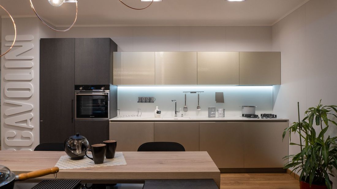 Una cucina moderna con eleganti mobili beige, un forno grigio scuro, un tavolo da pranzo in legno e una pianta verde in vaso.