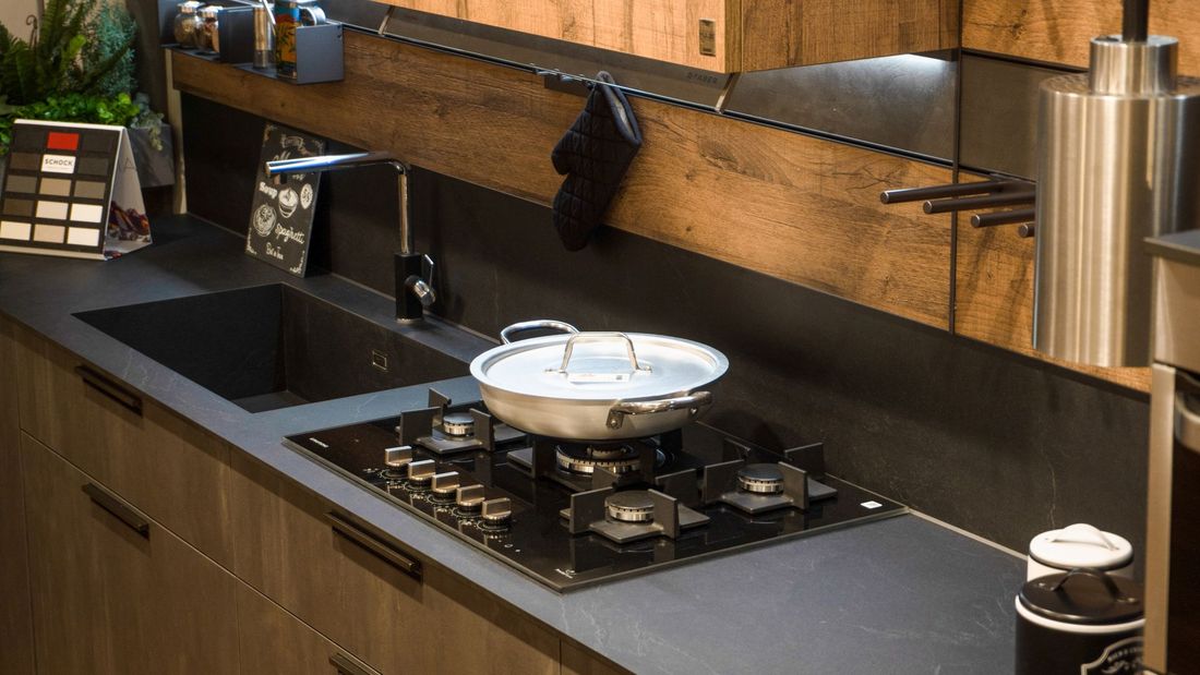 Una cucina moderna con piano di lavoro scuro con lavello integrato, piano cottura a gas con padella e mobili in legno.