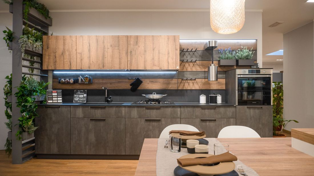 Cucina moderna con mobili base grigi, pensili in legno, elettrodomestici integrati e piante decorative.