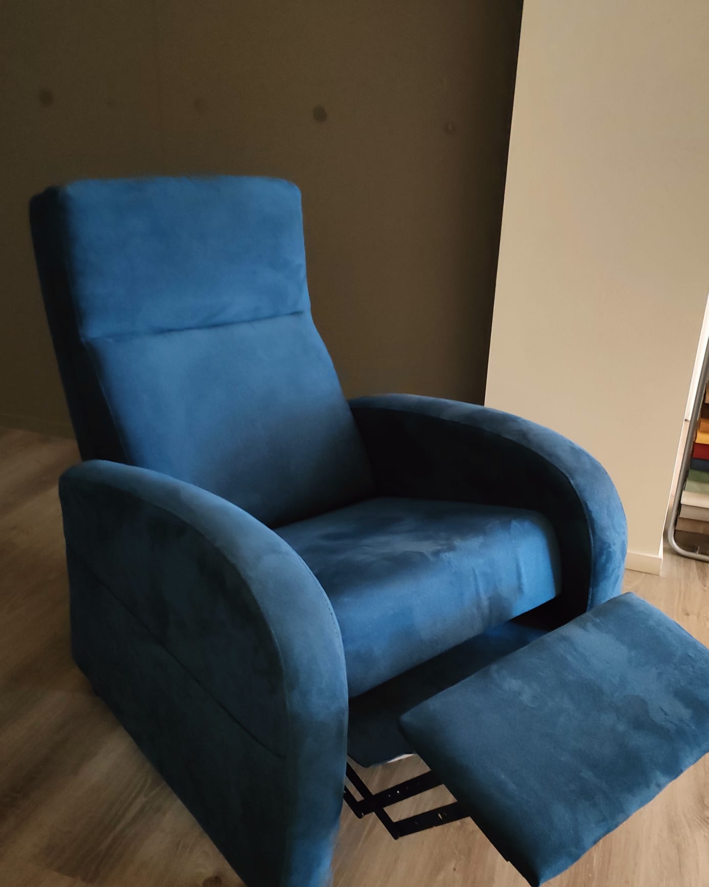 Una poltrona reclinabile in tessuto blu acceso, in posizione rialzata, è posizionata su un pavimento in legno chiaro all'interno di una stanza.