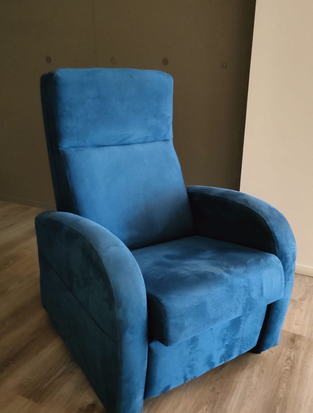 Una poltrona imbottita blu con schienale alto e braccioli arrotondati, posizionata su un pavimento in legno chiaro.