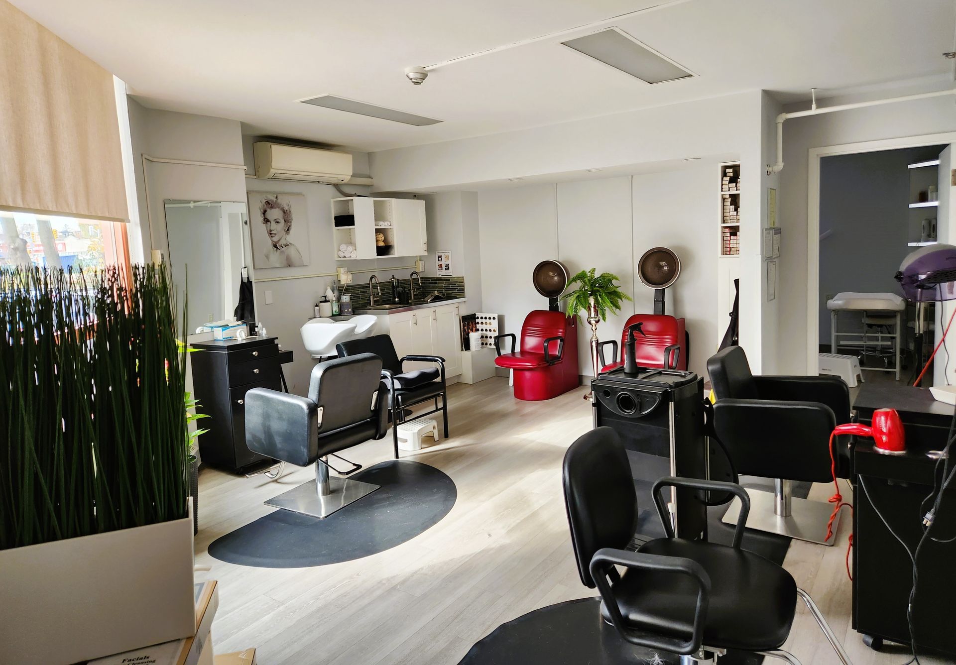 Interior of a hair salon with styling chairs, sinks, and hair dryers. White walls and light wood floors.