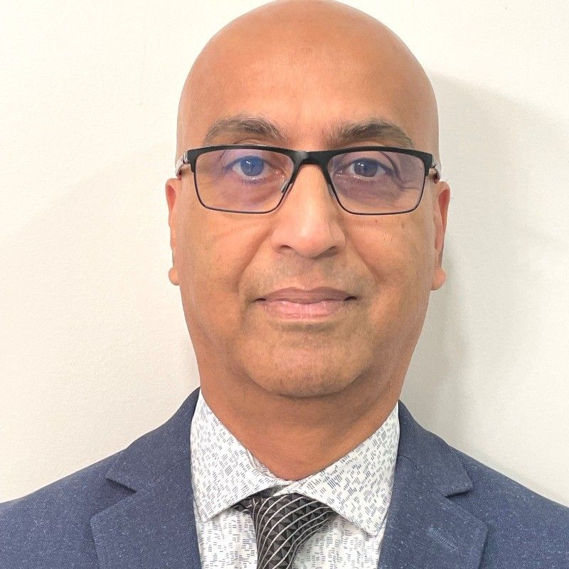 Bald man wearing glasses, suit, and tie, looking at the camera.