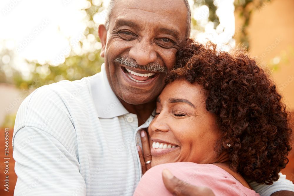 Smiling couple embracing outdoors. The man wears a light polo, the woman a pink top.