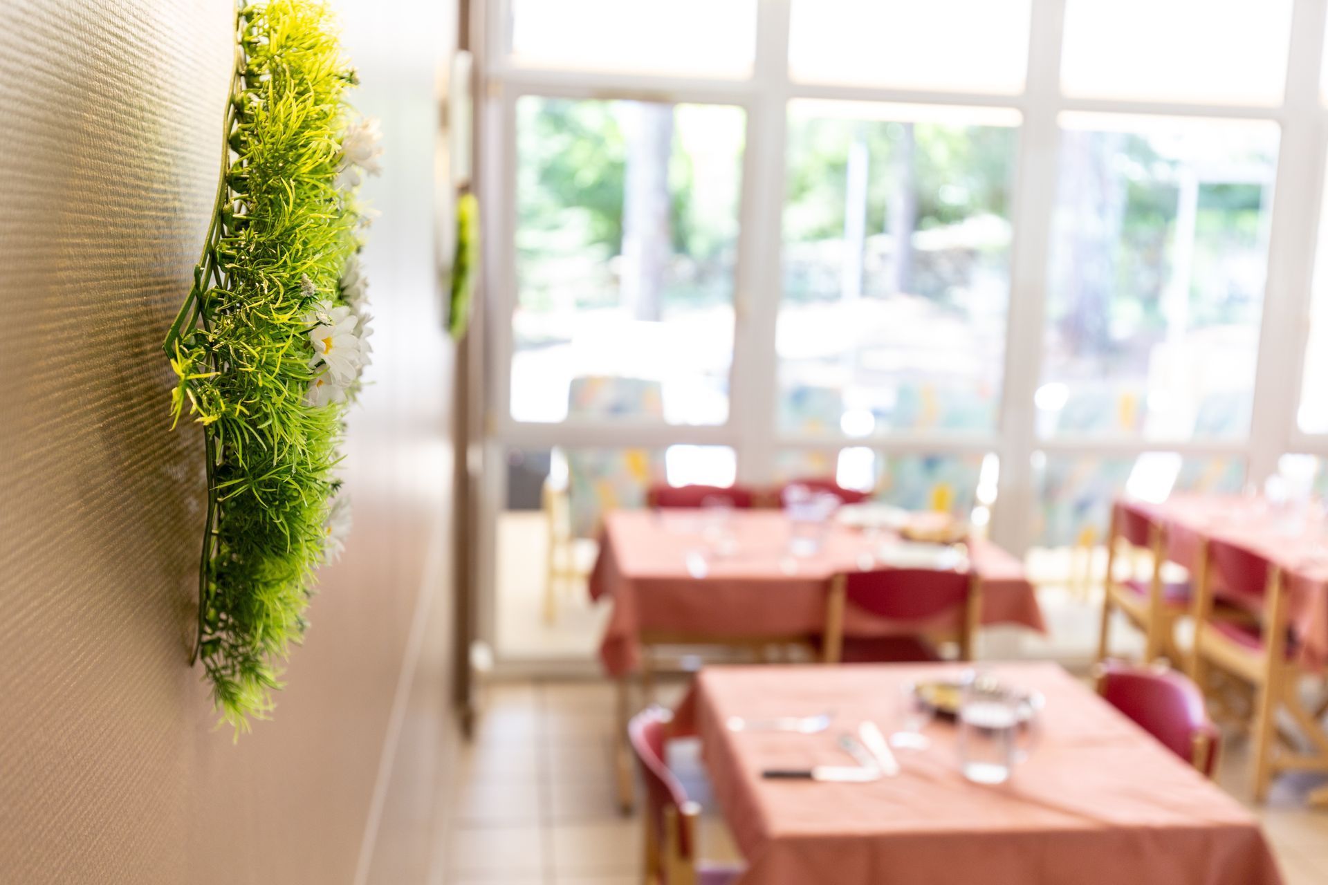 A dining room with tables and chairs and a plant on the wall.