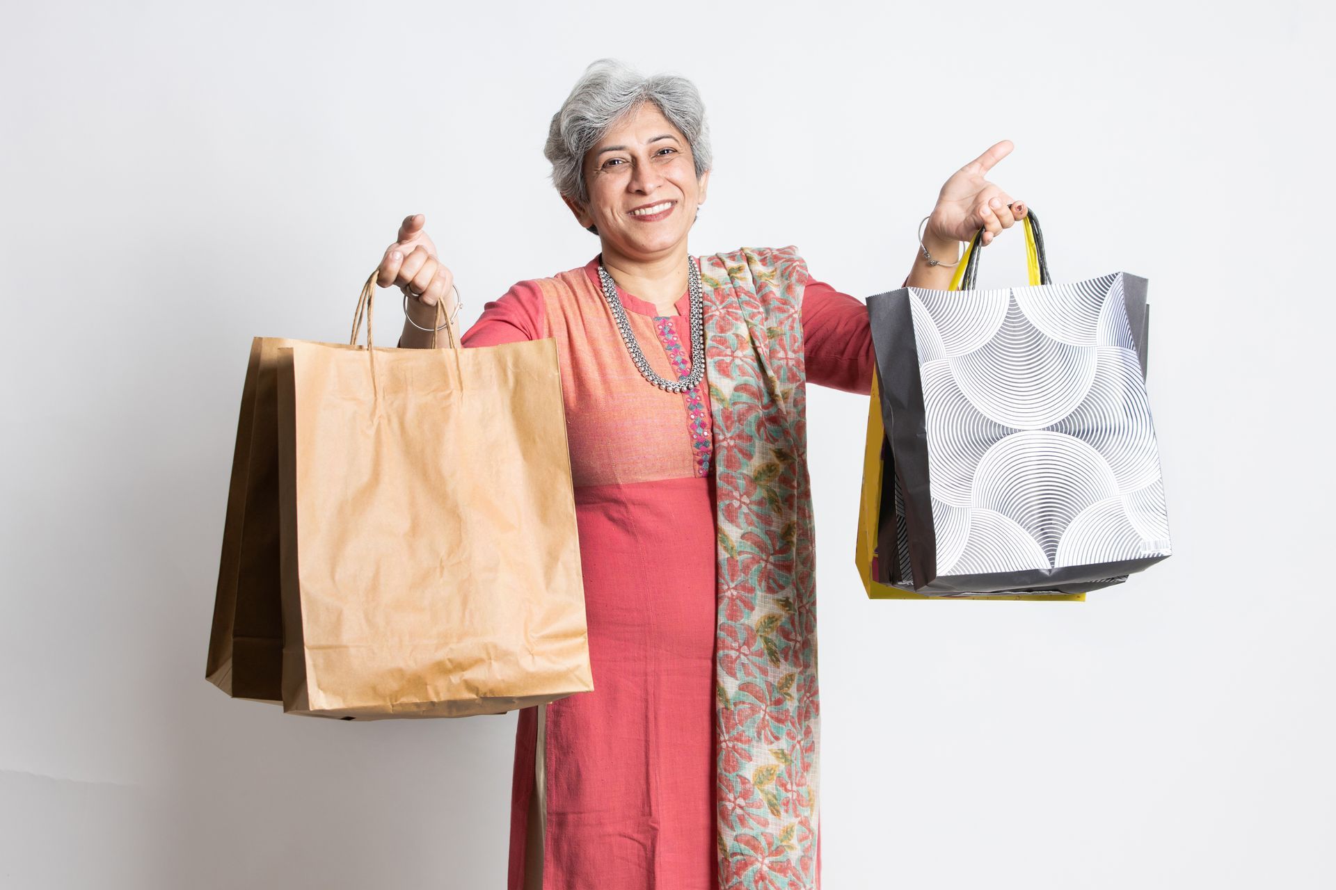 Smiling person with grey hair holding two shopping bags, against a white background.