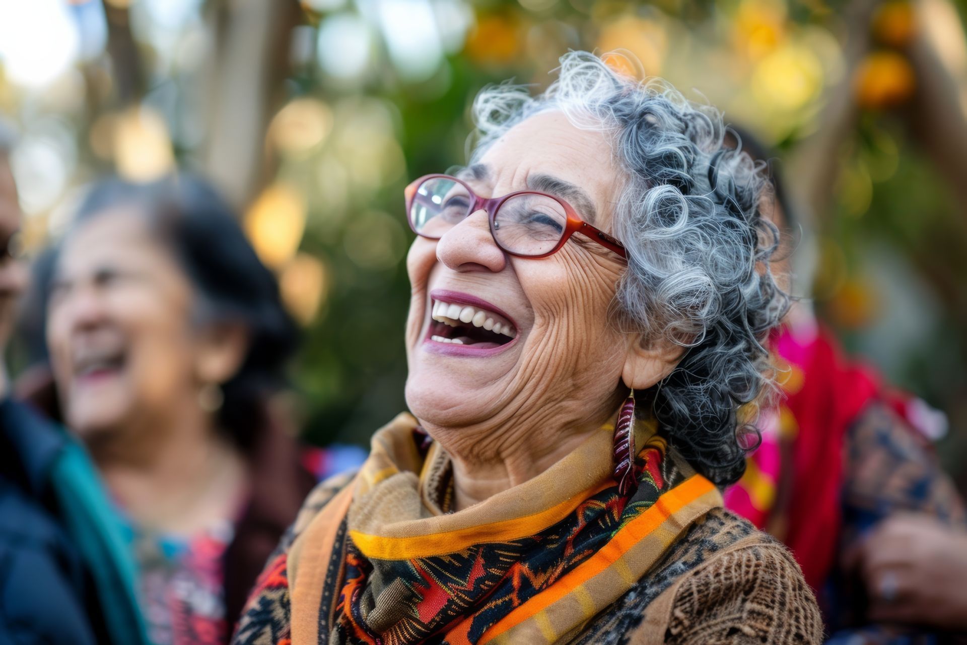 Woman with glasses and gray hair laughing outdoors, surrounded by others.