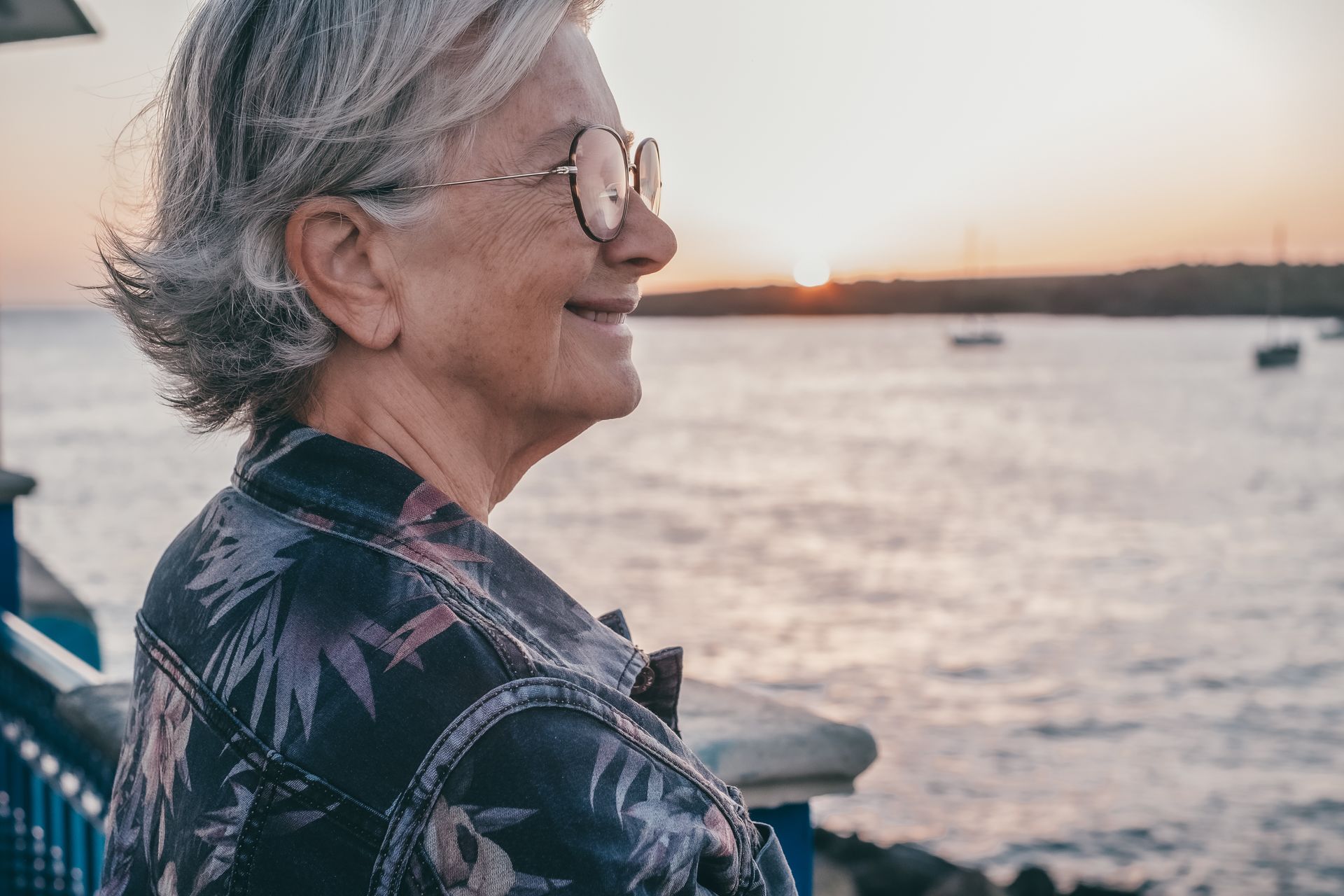 Woman in glasses gazes at sunset over water. She smiles.