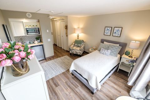Cozy studio apartment with a bed, small kitchenette, patterned rug, and floral decorations.