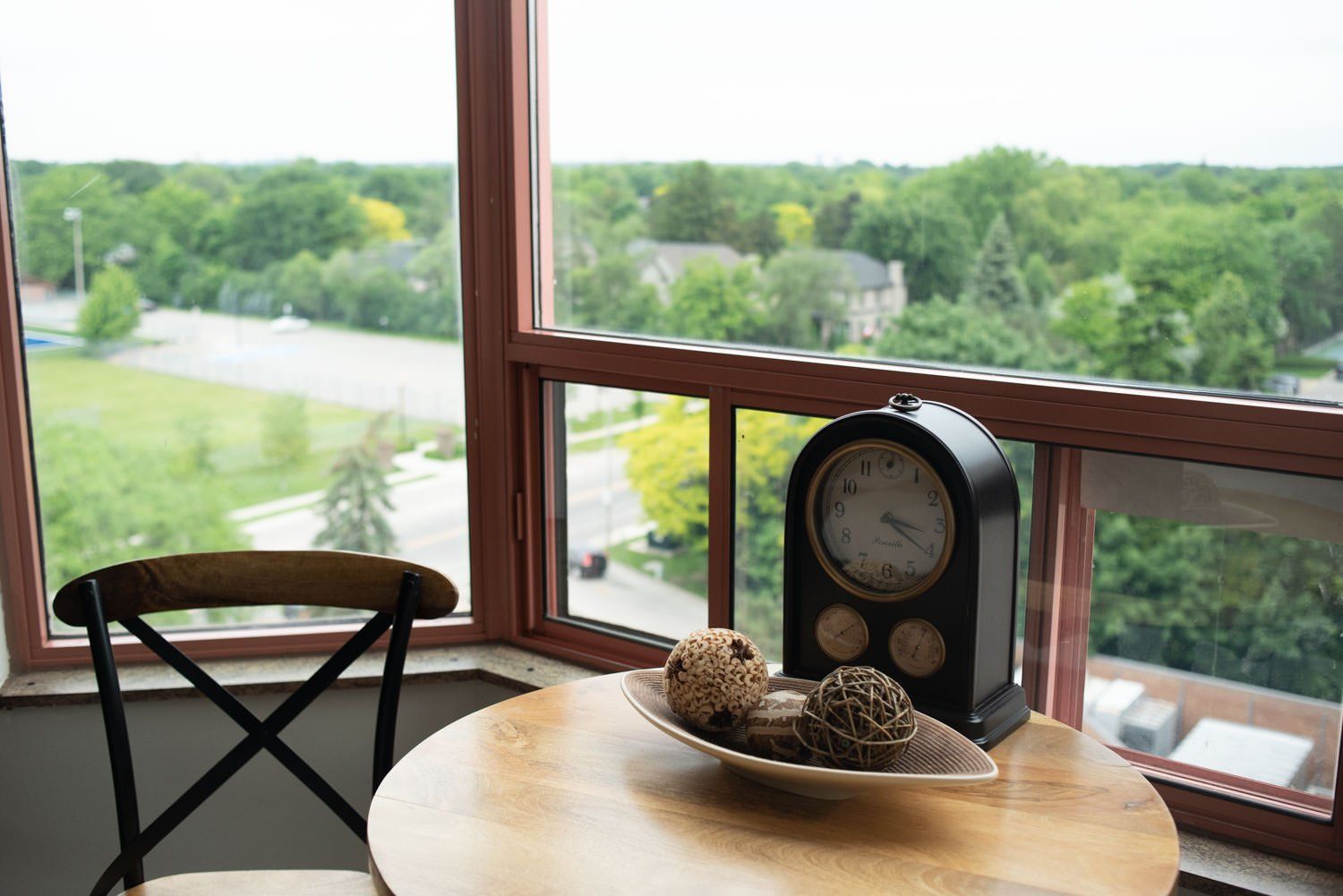 Corner window with a round table, clock, and decorative balls, overlooking a green landscape.