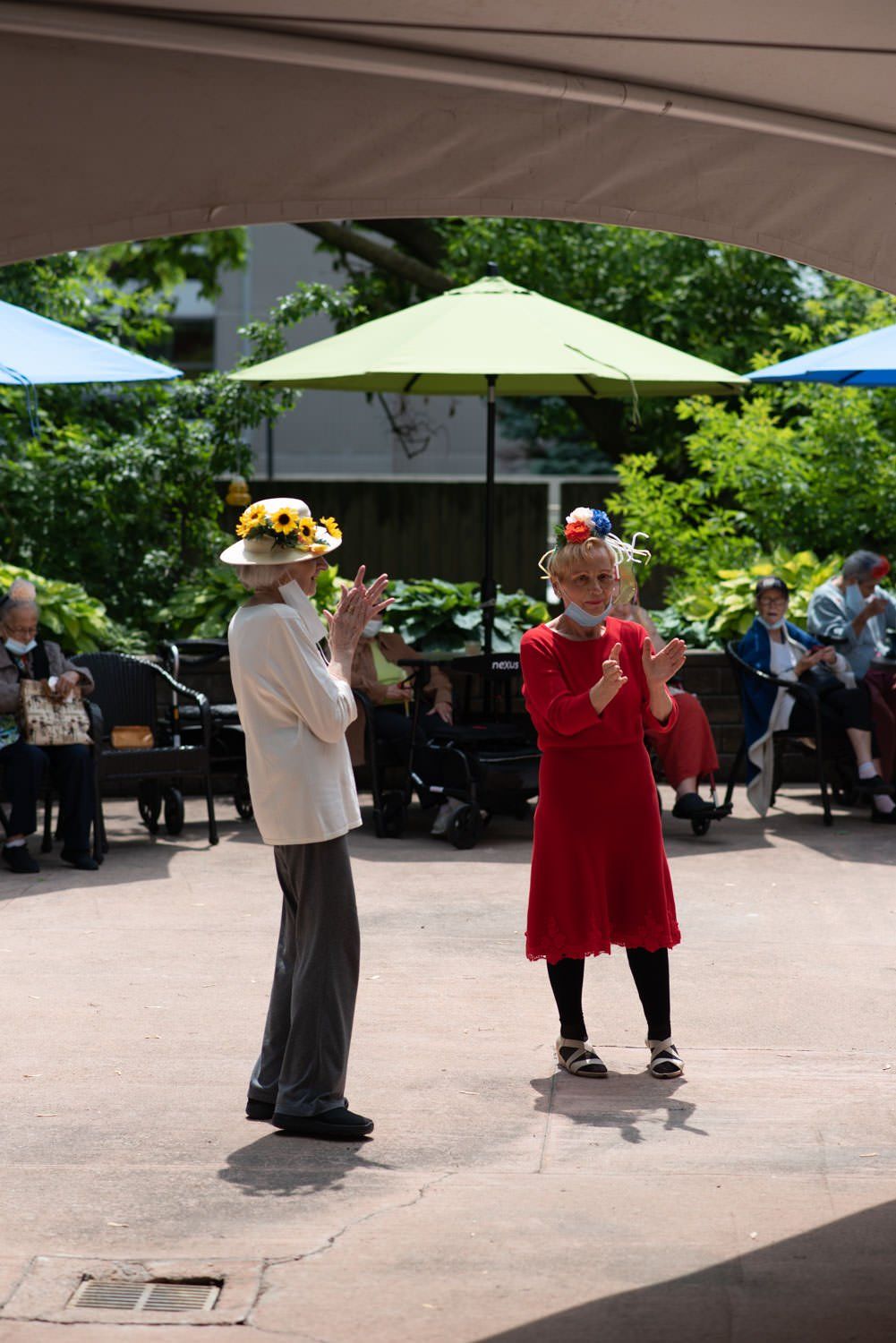 Two people in hats juggling outside, surrounded by onlookers.