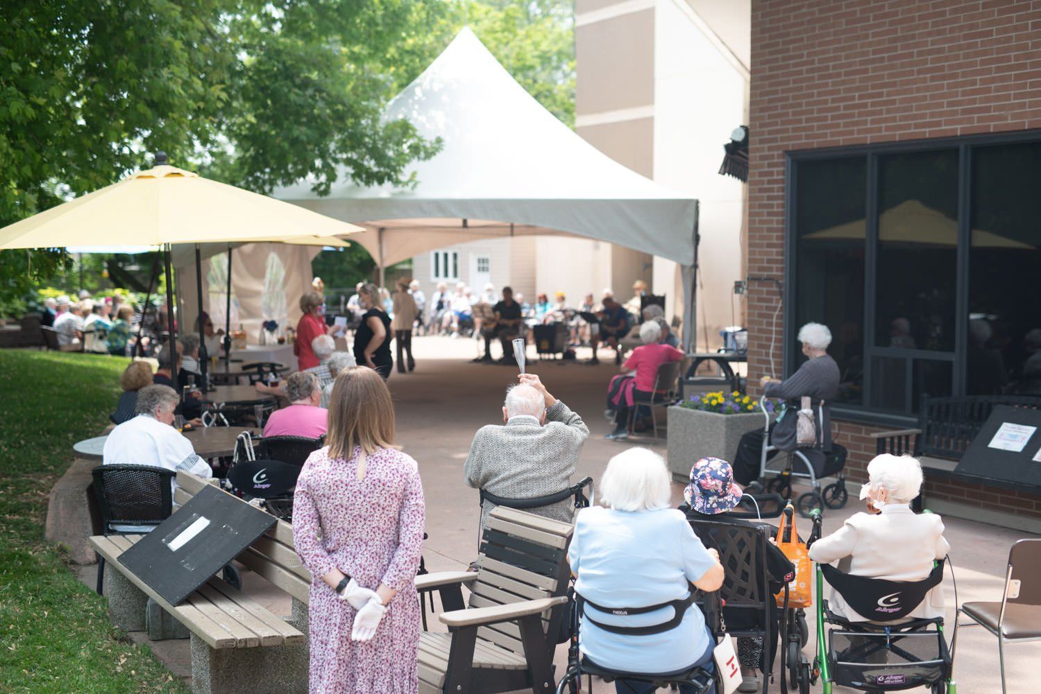People gathered outdoors under tents and umbrellas, possibly at an event.