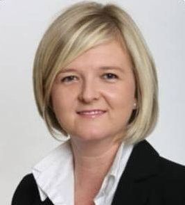 Woman with blonde bob and white collared shirt smiling.