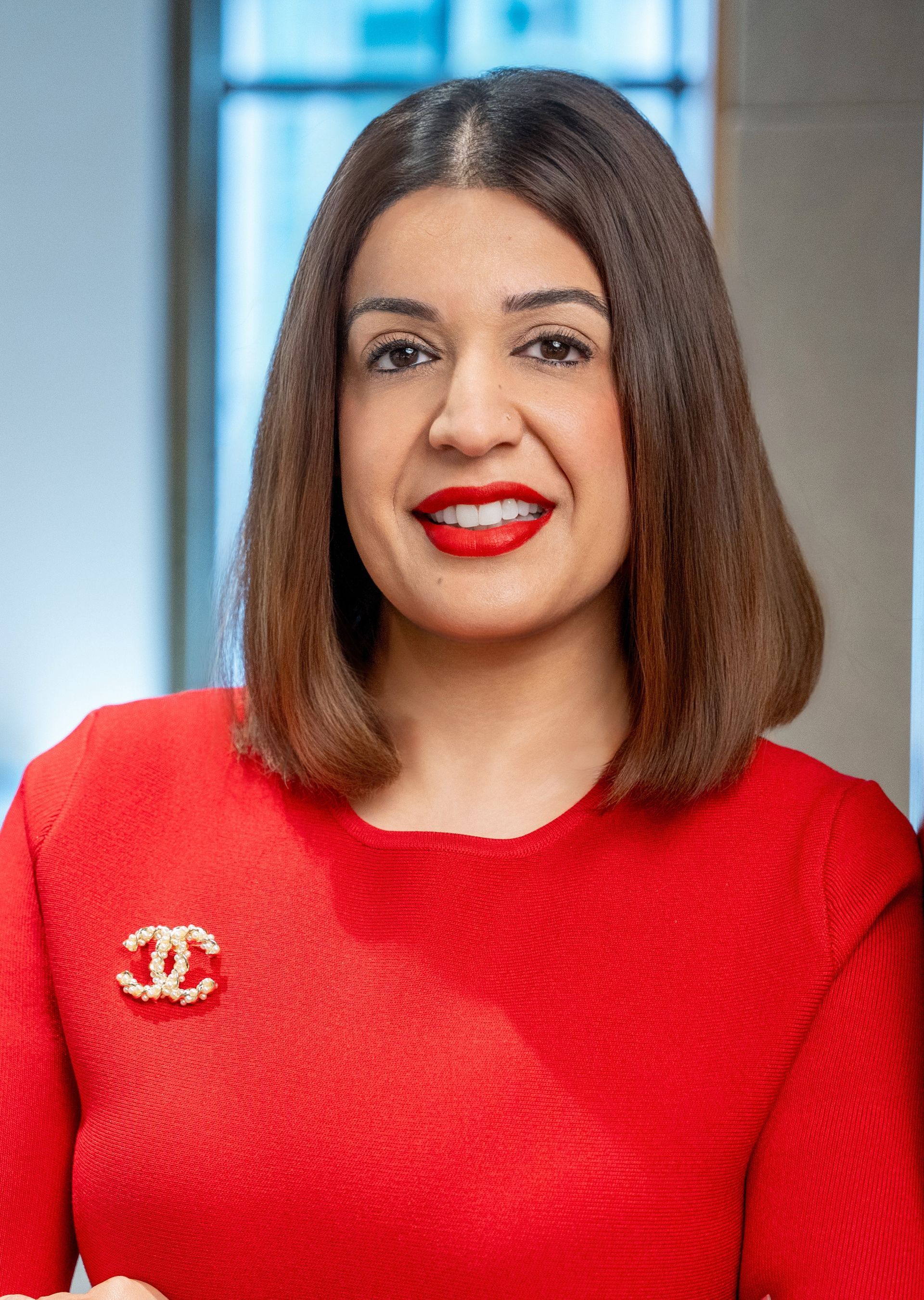 Woman in red dress with Chanel brooch, red lipstick; smiling.
