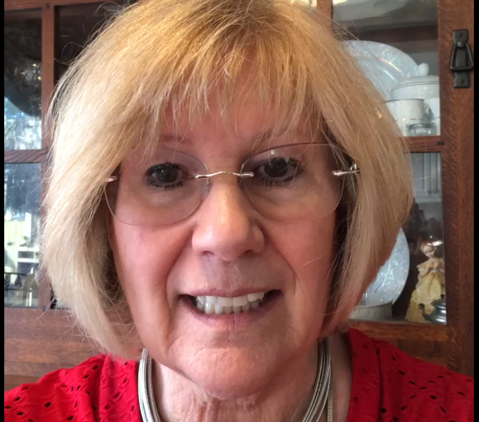 Woman with short blonde hair, wearing glasses and a red shirt, smiling.