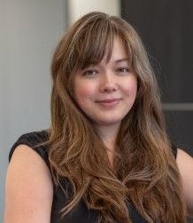 Woman with long brown hair smiling. Black top.