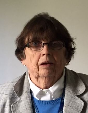 Woman with short brown hair, glasses, and a gray blazer looks directly at the camera.