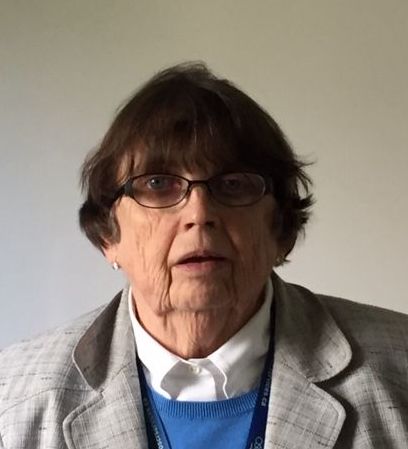Woman wearing glasses and a light blazer, looking forward with a neutral expression.