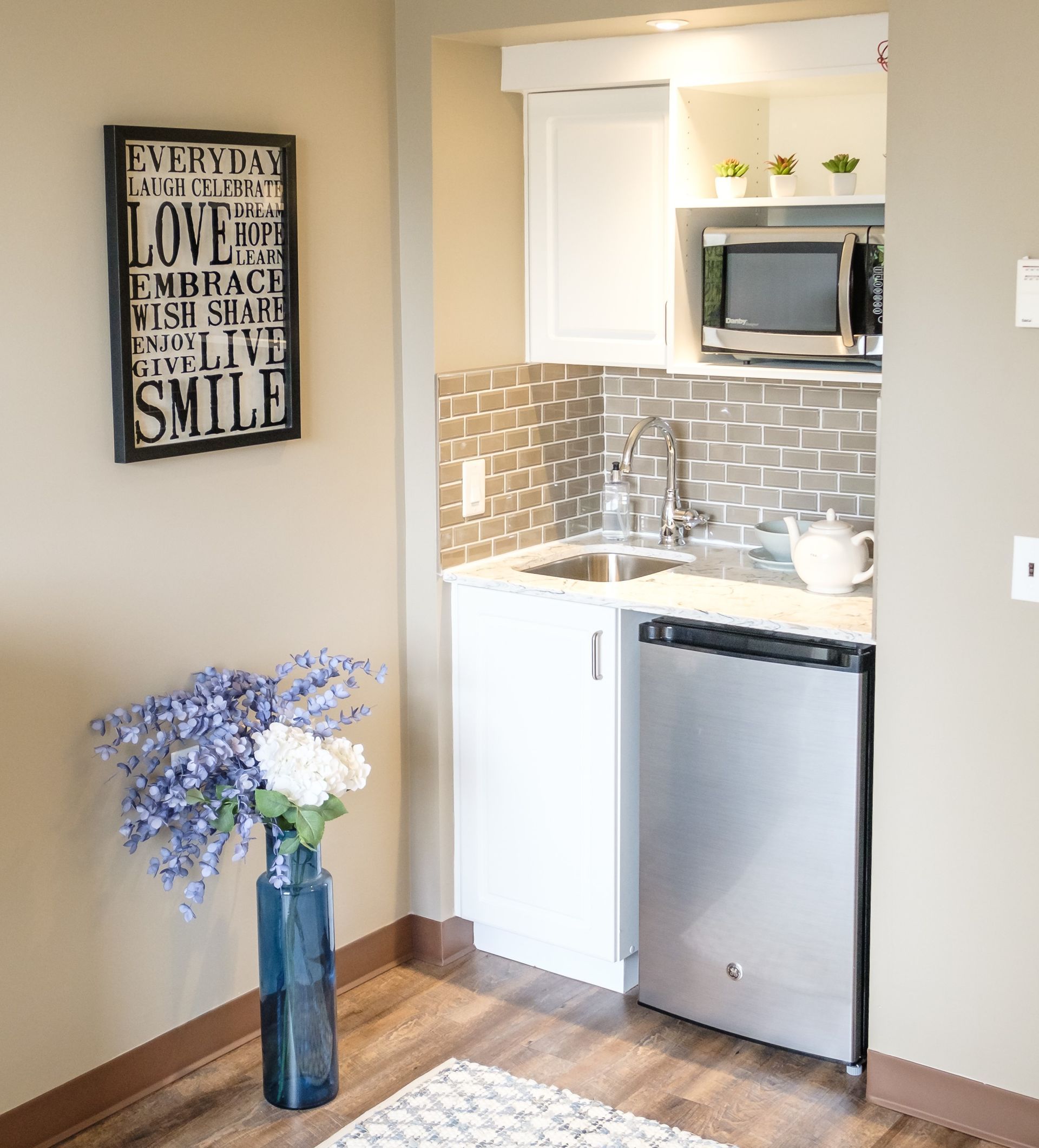 Small kitchenette with white cabinets, stainless steel appliances, and decorative tile backsplash.