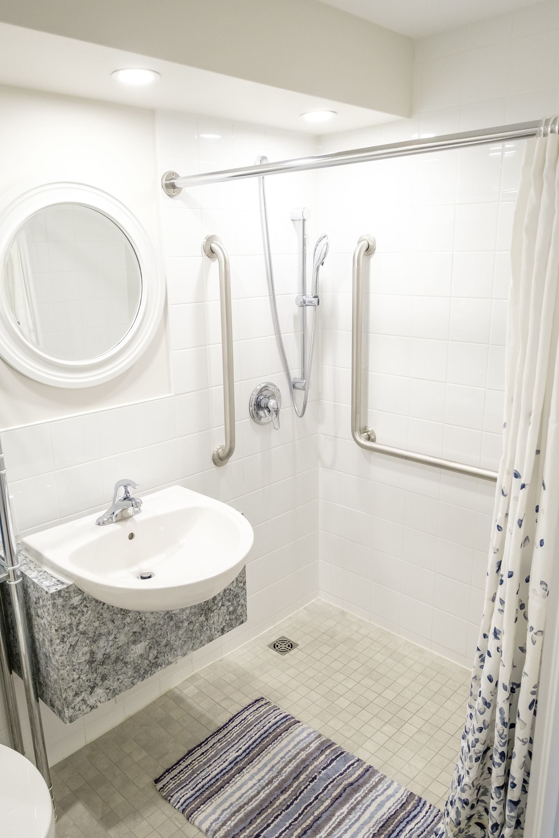 Accessible bathroom with a sink, shower, and safety bars. White and gray tones.