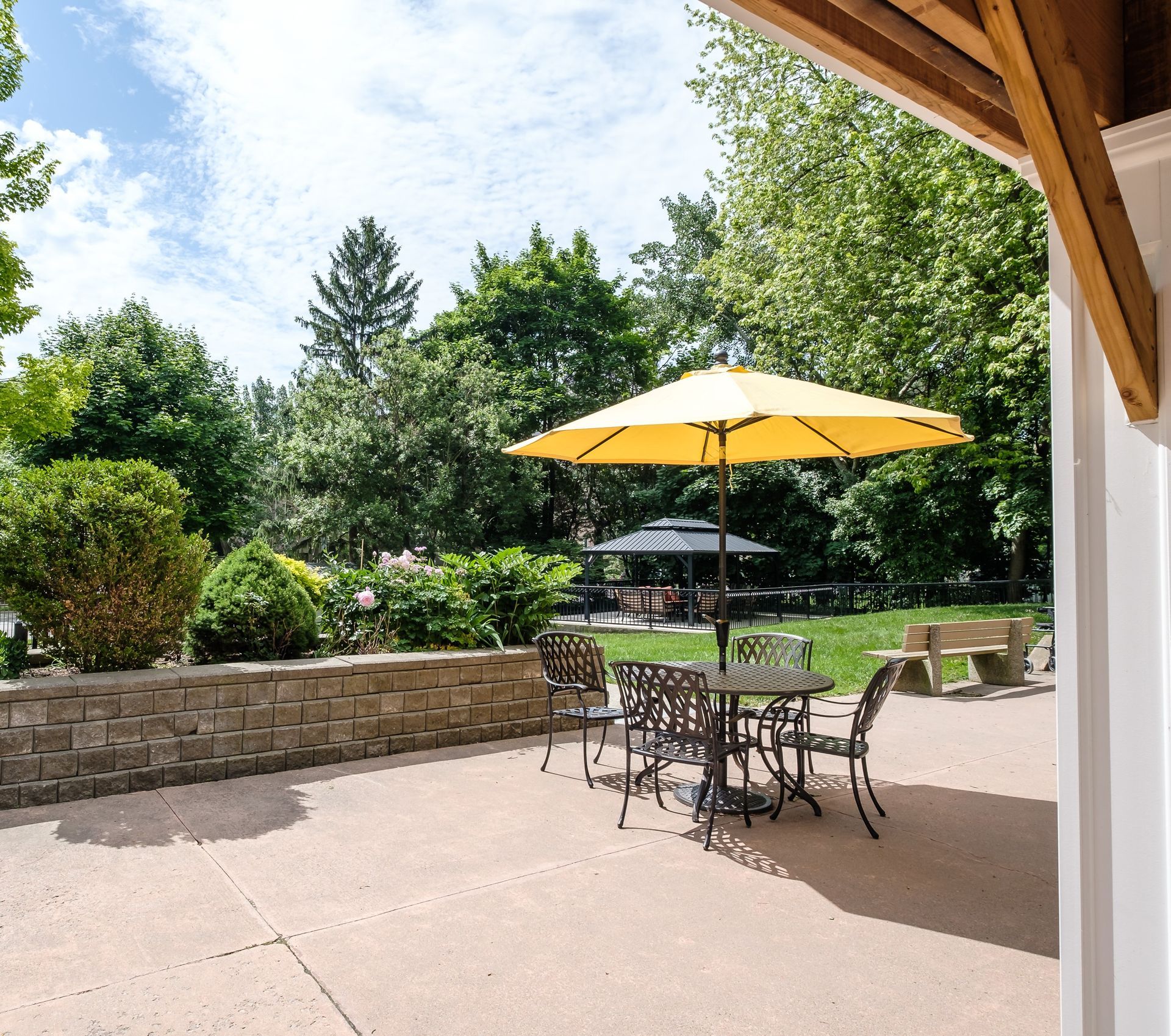 Patio with yellow umbrella, table, chairs, and stone wall, overlooking a yard with trees.