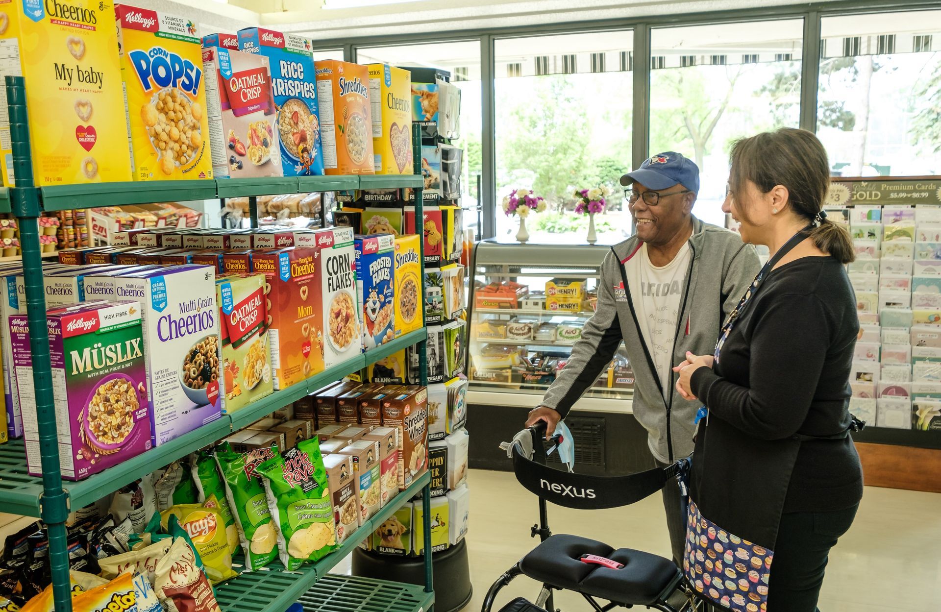 A person using a walker and another person stand in a store aisle with cereal.