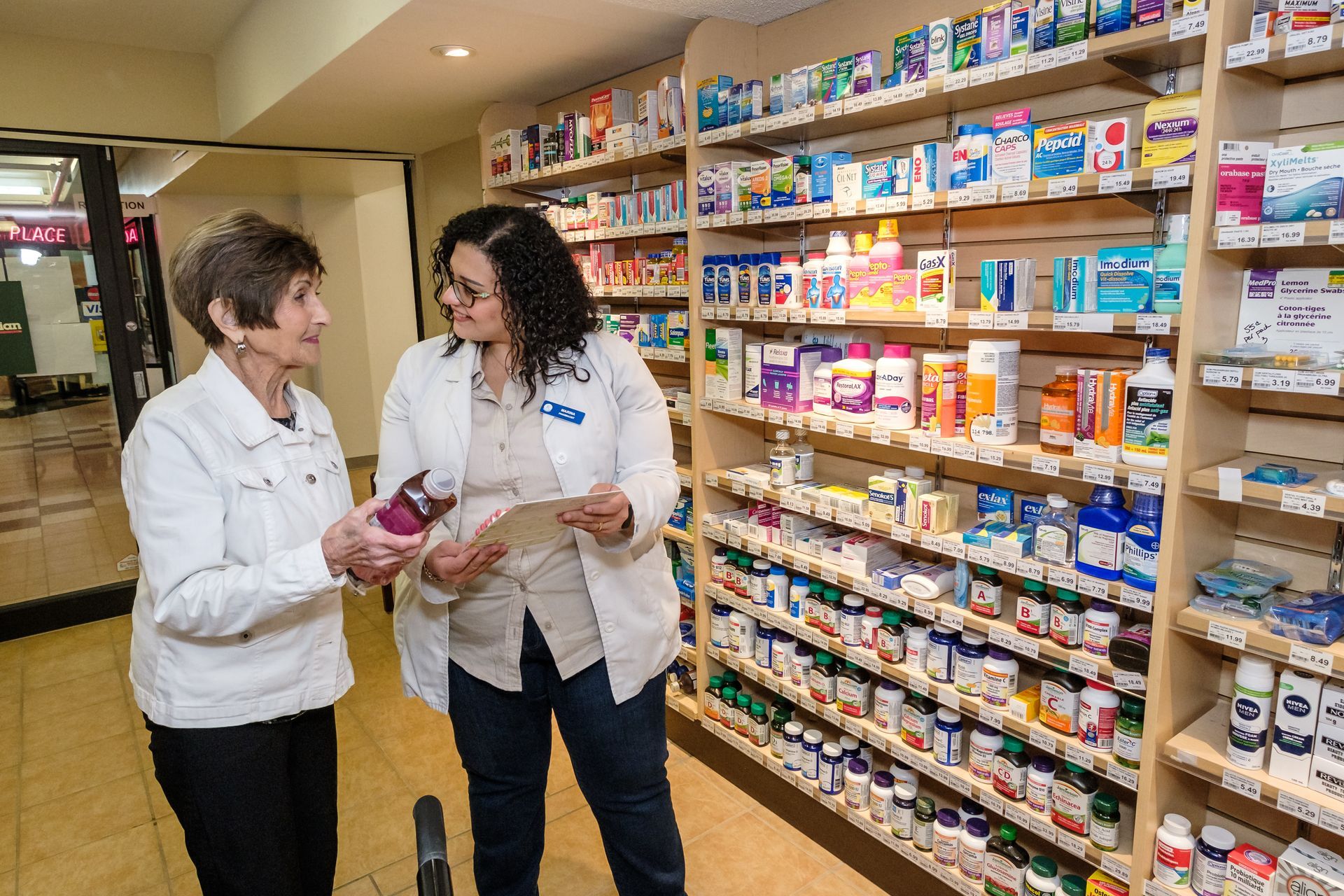 Pharmacist consulting with a customer in a pharmacy aisle, reviewing medication label.