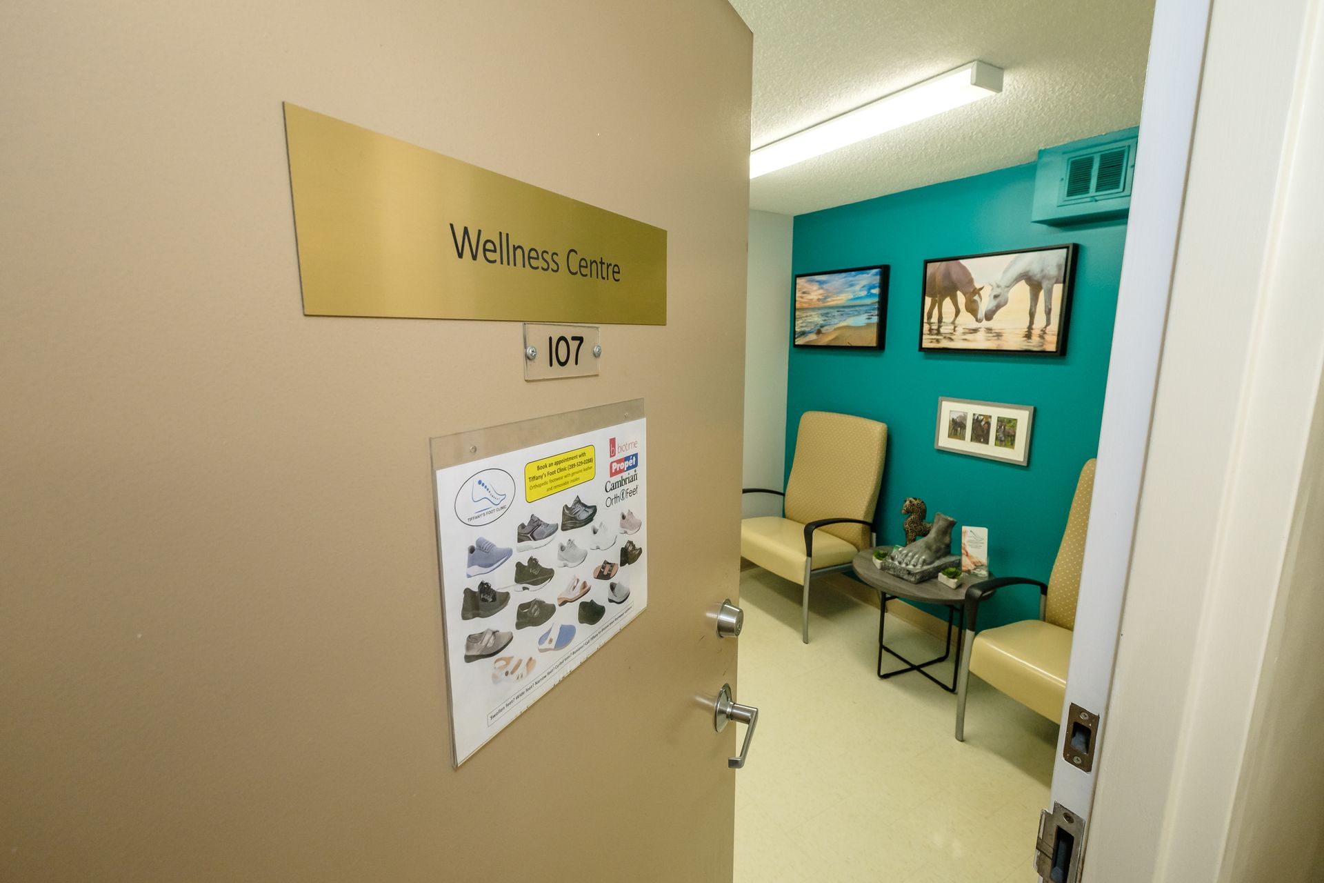 Door to Wellness Centre, beige walls, turquoise accent wall, framed art, two chairs, table, white door frame.