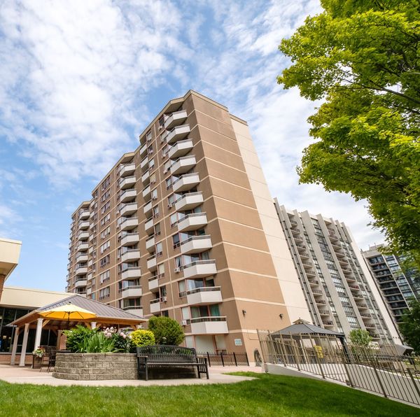 Multi-story tan apartment building with balconies, sunny day, green grass, gazebo.