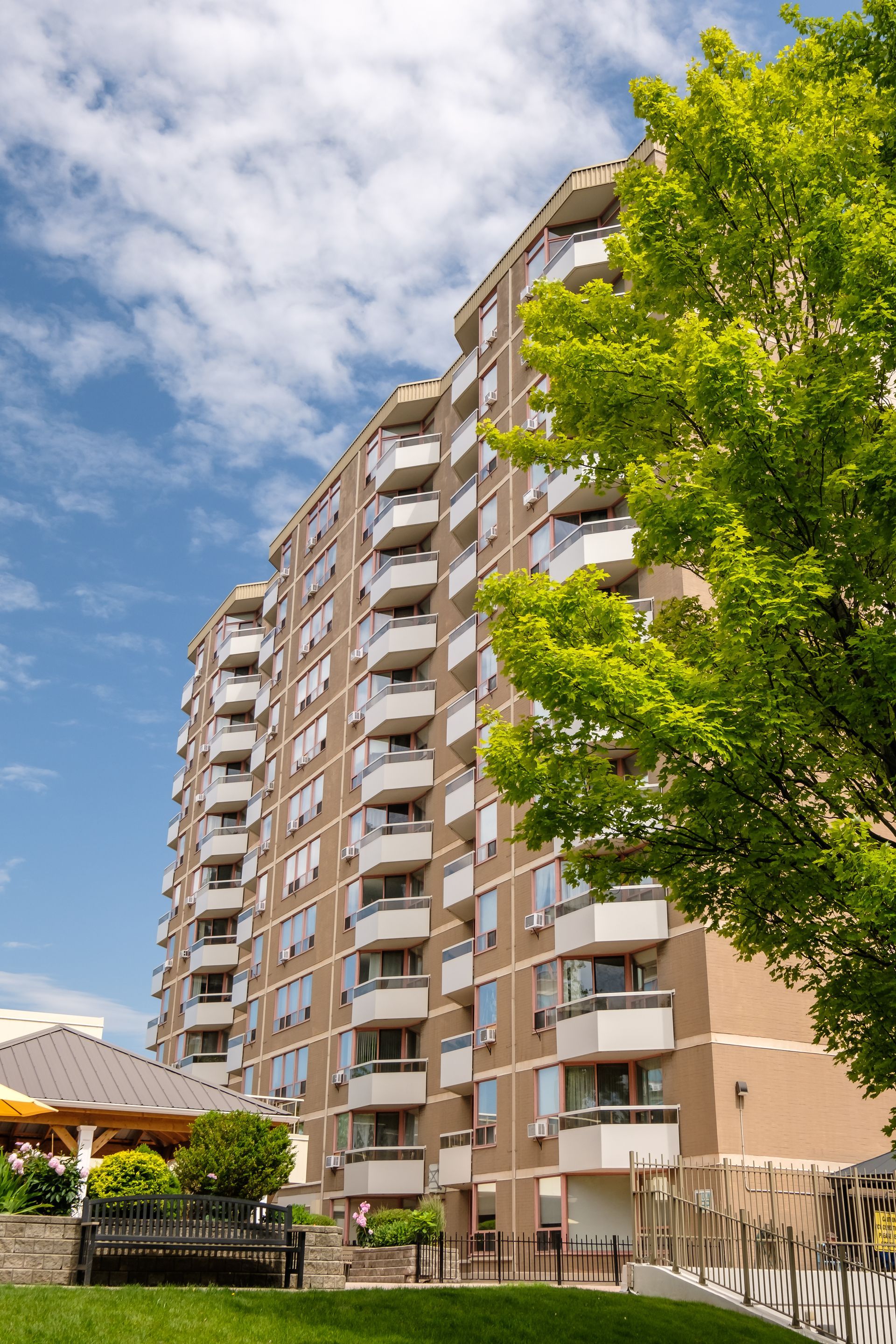 Tall tan apartment building with multiple balconies, under a blue sky with some clouds.