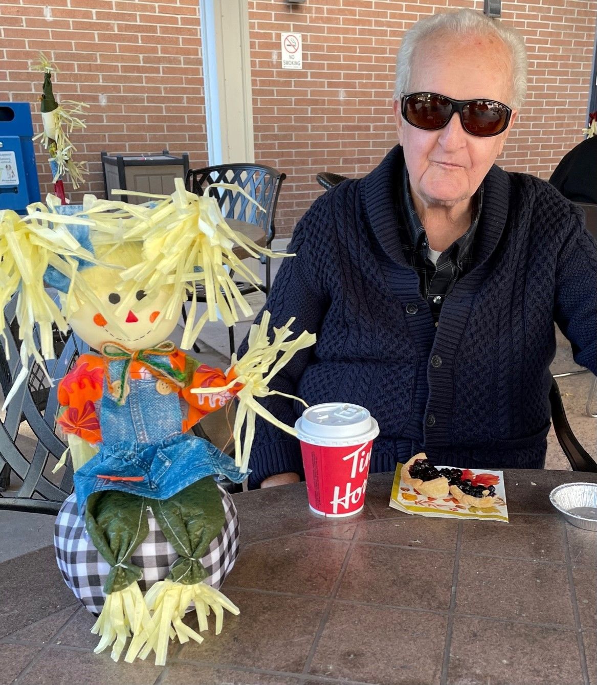 A man is sitting at a table with a scarecrow and a tim hortons cup