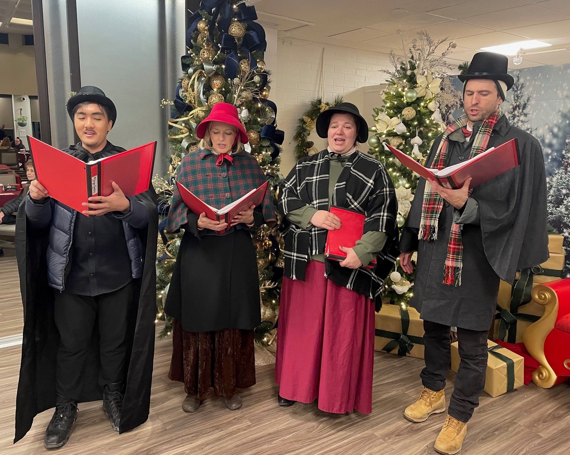 A group of people are singing christmas carols in front of a christmas tree.