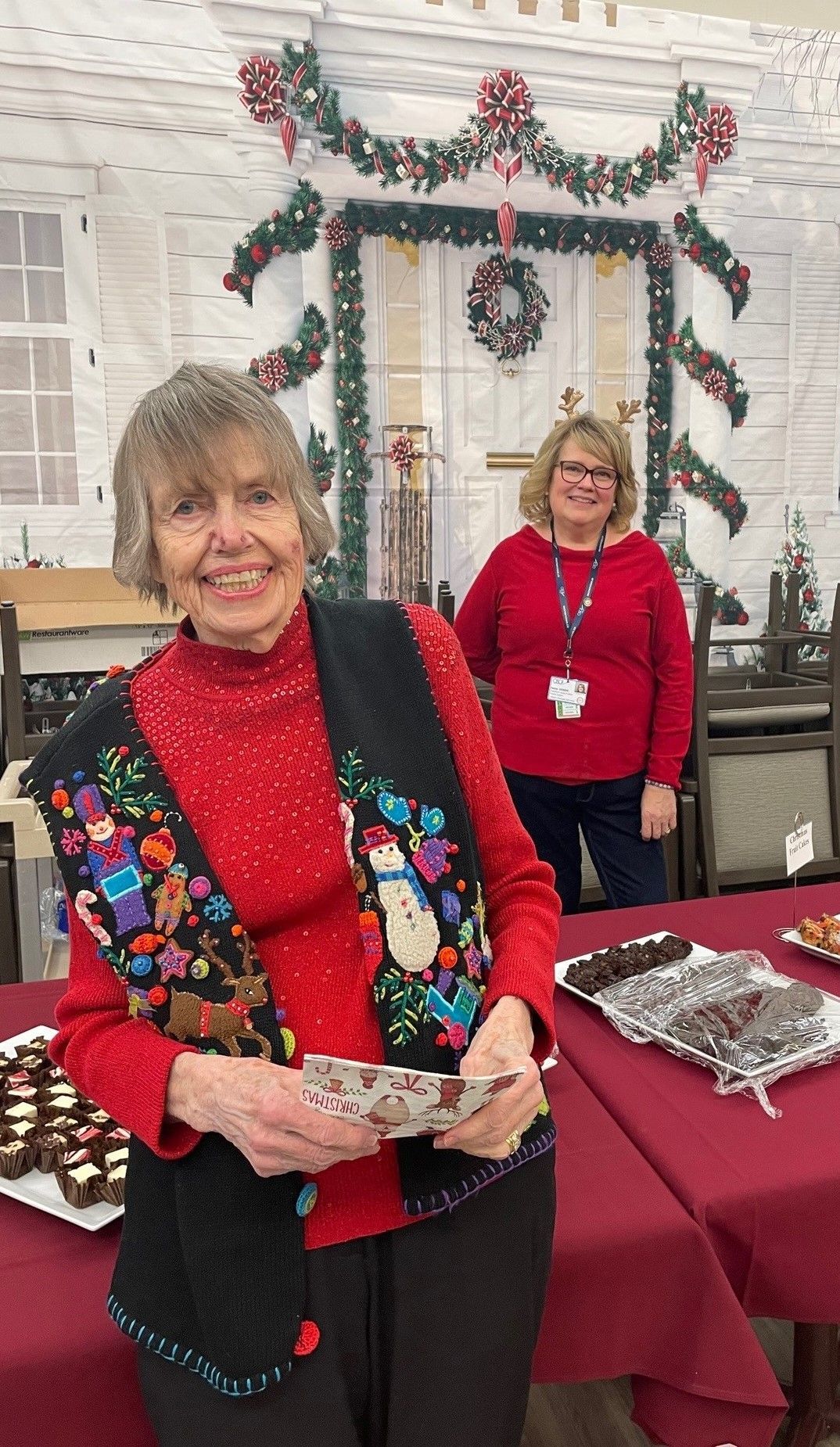 A woman in a red sweater is standing in front of a table holding a plate of food.