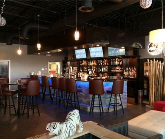 Cozy bar interior with hanging lights, stools, TV screens, and a zebra figurine in the foreground