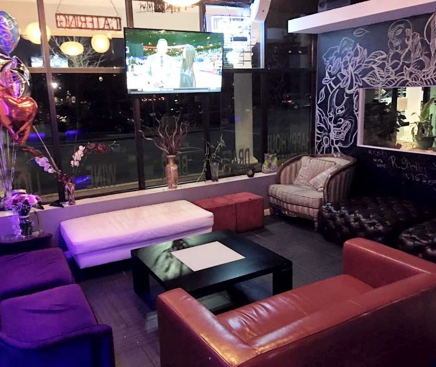 Colorful lounge with red sofas, black tables, purple lighting, and a TV on the wall