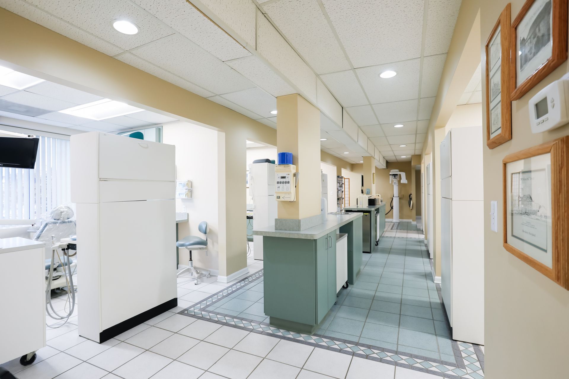 Bright hospital corridor with check-in desks, tiled floor, and framed certificates on the wall.