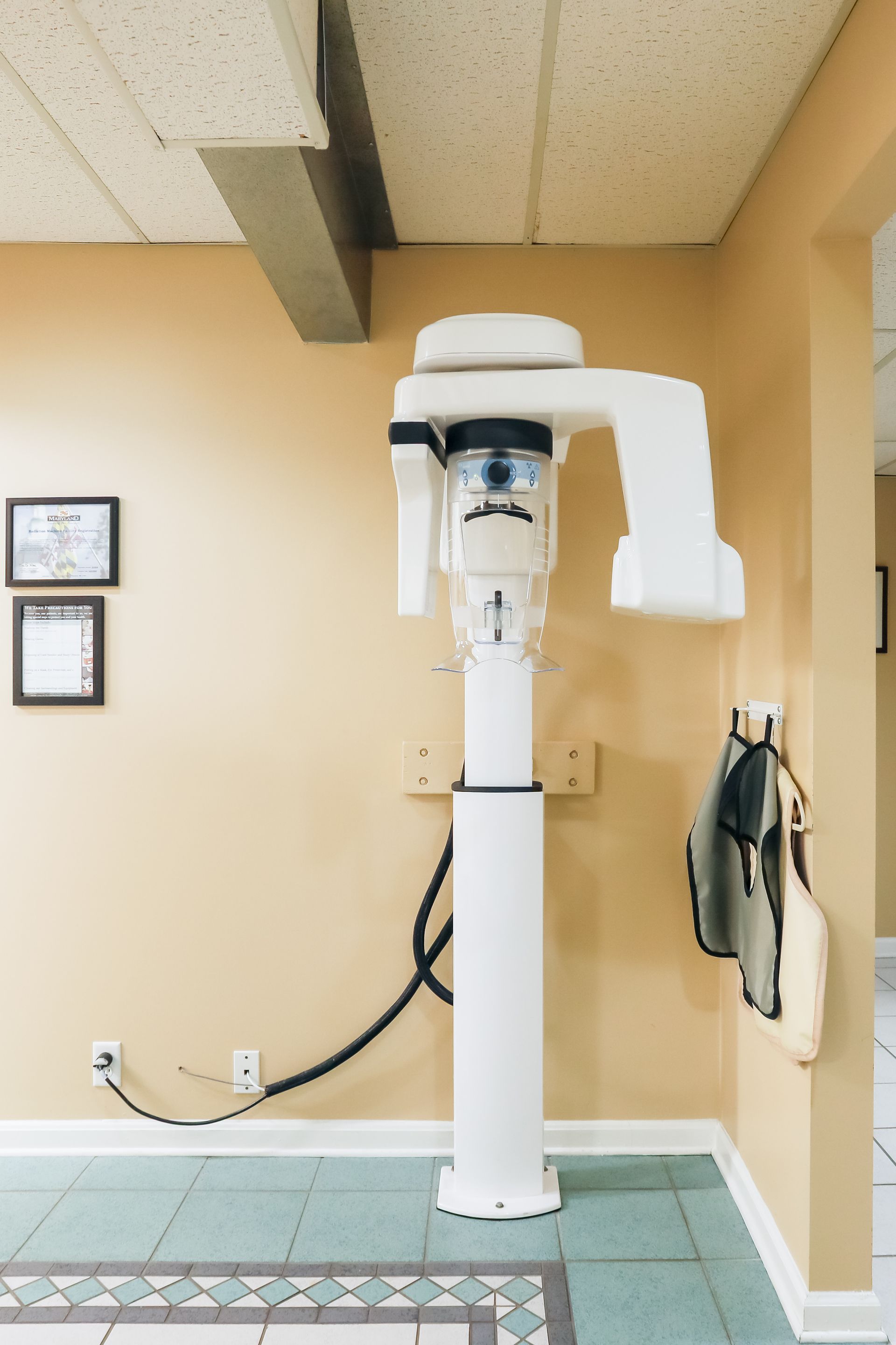 Dental X-ray machine in a clinic room with beige walls and tiled floor
