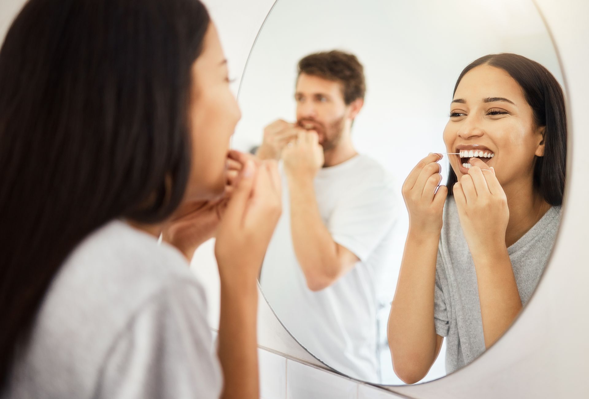 Two people brushing their teeth in a bathroom, smiling in a mirror.