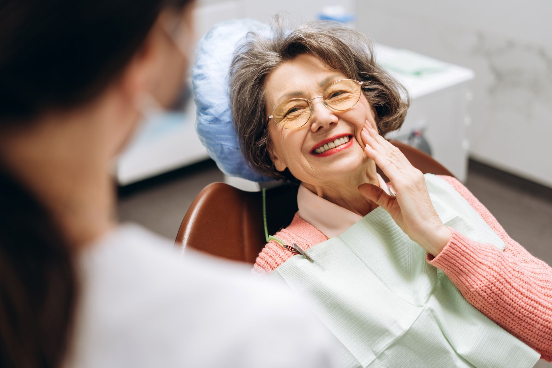 A dentist is looking at a patient 's smile in a mirror.