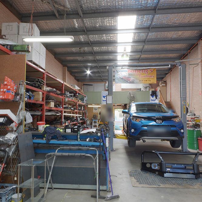 A Blue Car Is on A Lift in A Garage — Bonetig's Mobile Towbars & Trailers In Oak Flats, NSW