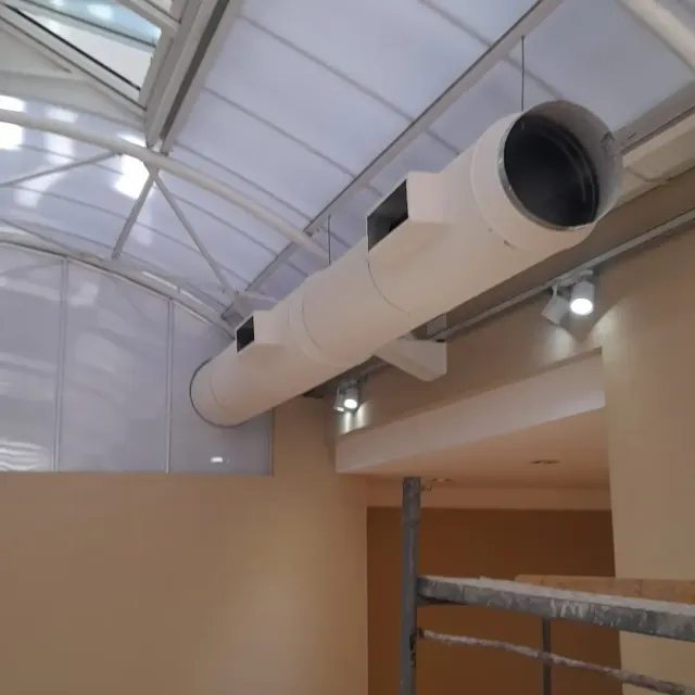 Conducto de ventilación blanco cerca de un techo de cristal en una zona de construcción interior.