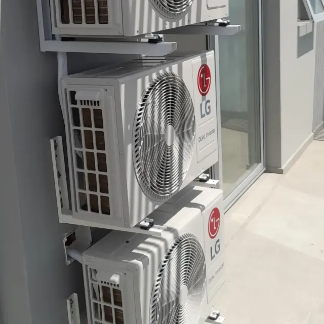 Unidades de aire acondicionado exteriores LG blancas apiladas e instaladas en la fachada de un edificio junto a una ventana.