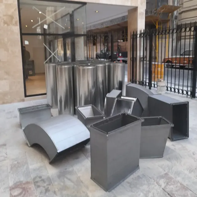 Conductos metálicos y piezas de sistemas de climatización apilados en una acera frente a la entrada de un edificio.