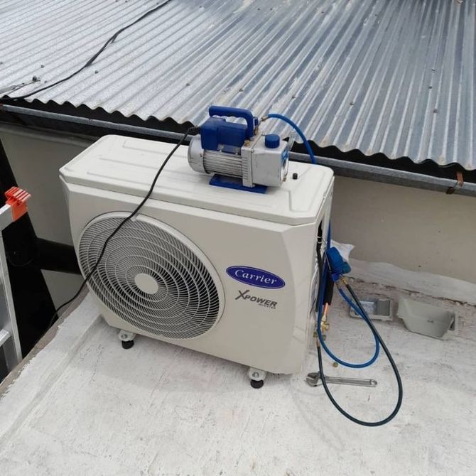 Unidad exterior de aire acondicionado blanca con equipo azul acoplado en una azotea junto a un techo de chapa ondulada.