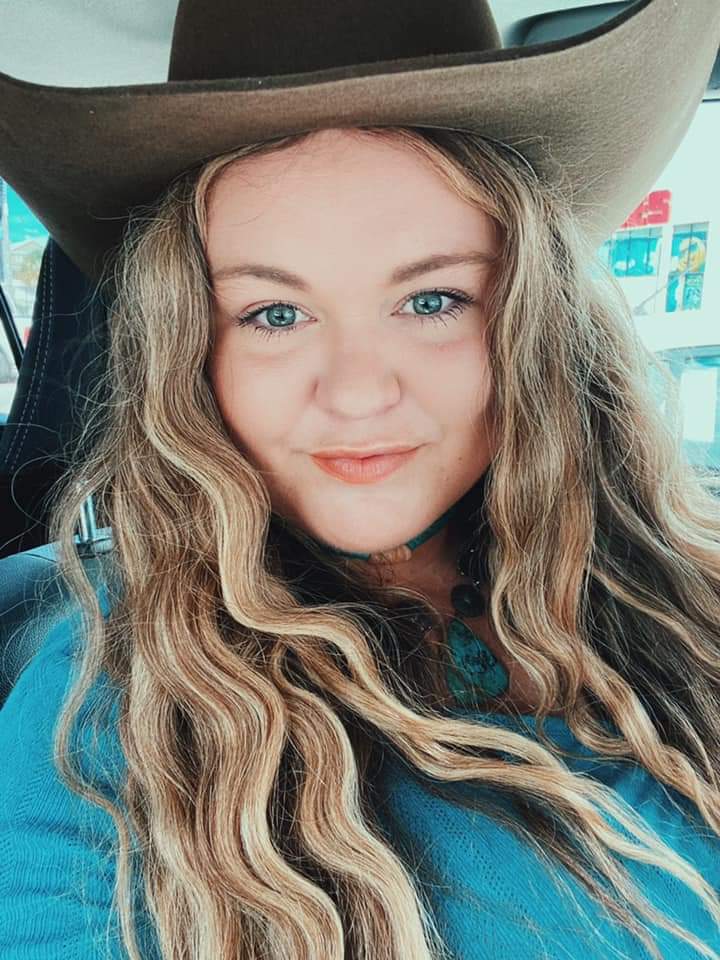A woman wearing a cowboy hat and a blue shirt is sitting in a car.