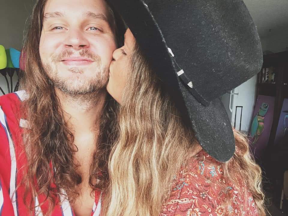 A woman is kissing a man on the cheek while wearing a hat.